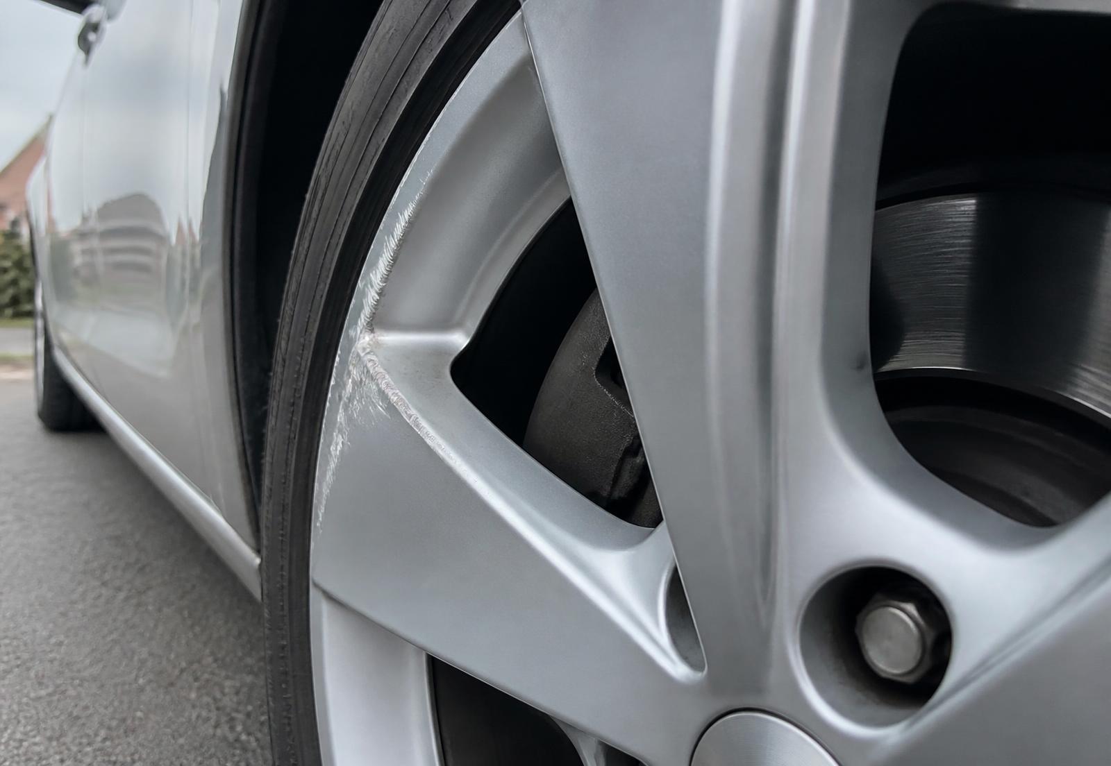 Close-up of a silver alloy wheel showing kerb rash along the rim edge
